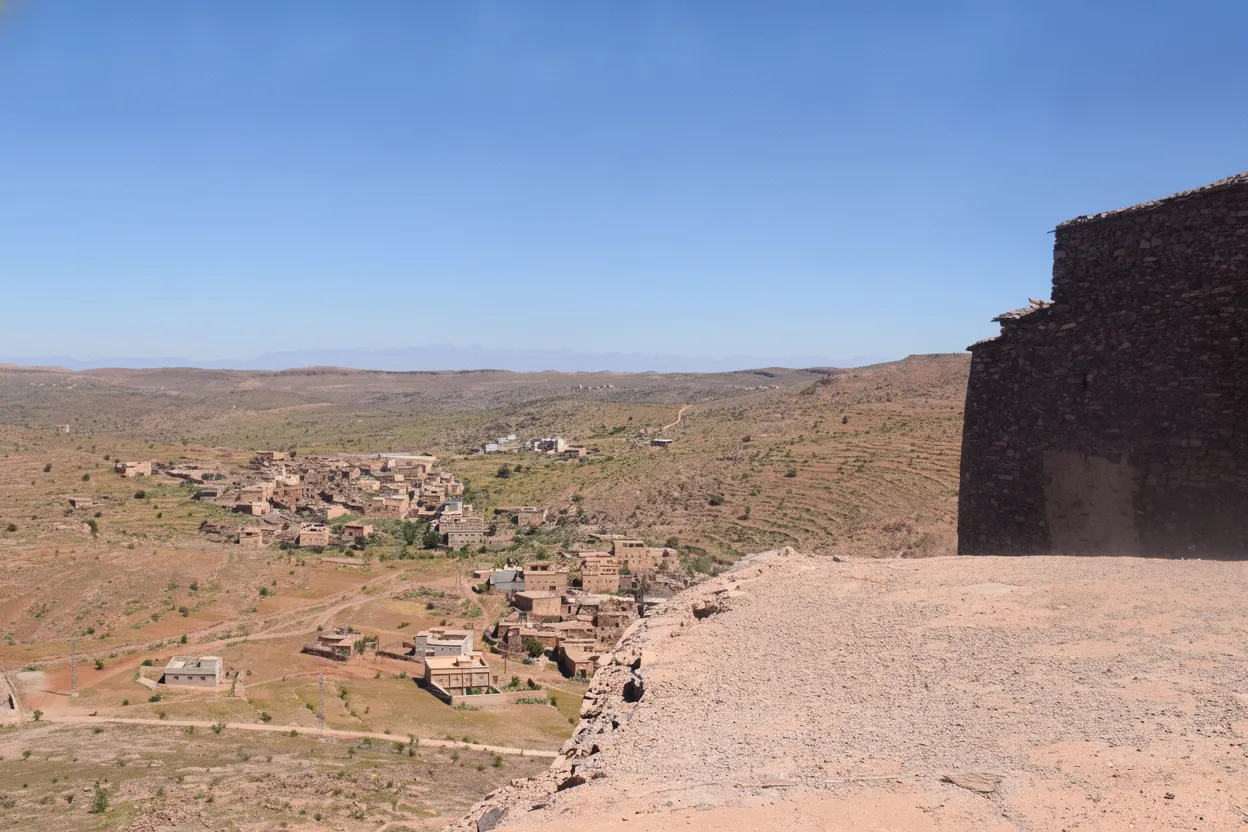 Panoramic view of Agadir Tasguent, a multi-story fortified granary carved directly into a rugged cliff face in the Anti-Atlas Mountains, Morocco, blending seamlessly with the rock.