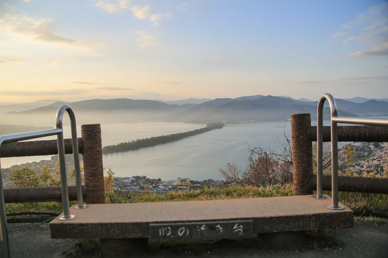 A serene view of a traditional Japanese boat cruising through Miyazu Bay with Amanohashidate sandbar in the background.