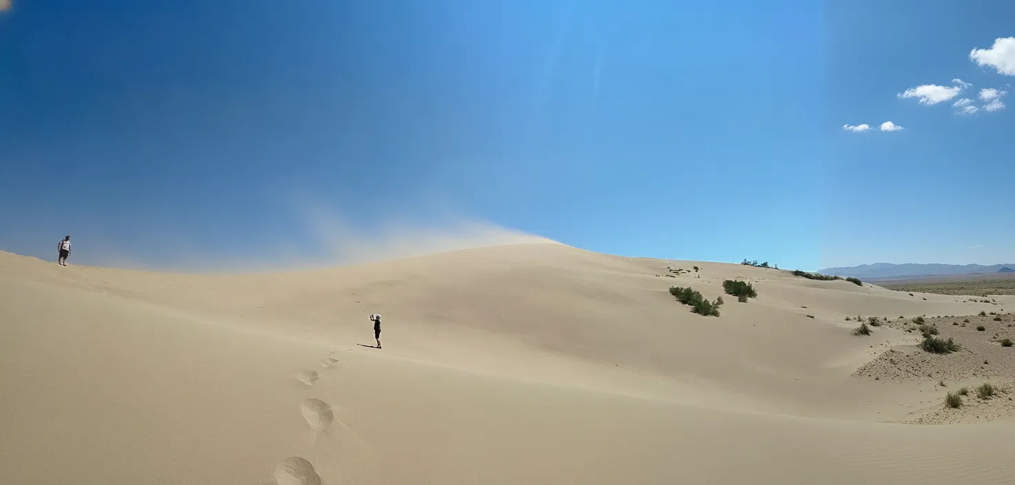 Panoramic view of the crescent-shaped Barkhan Ayyrkhan, the Singing Dunes, against a clear blue sky in Kazakhstan.
