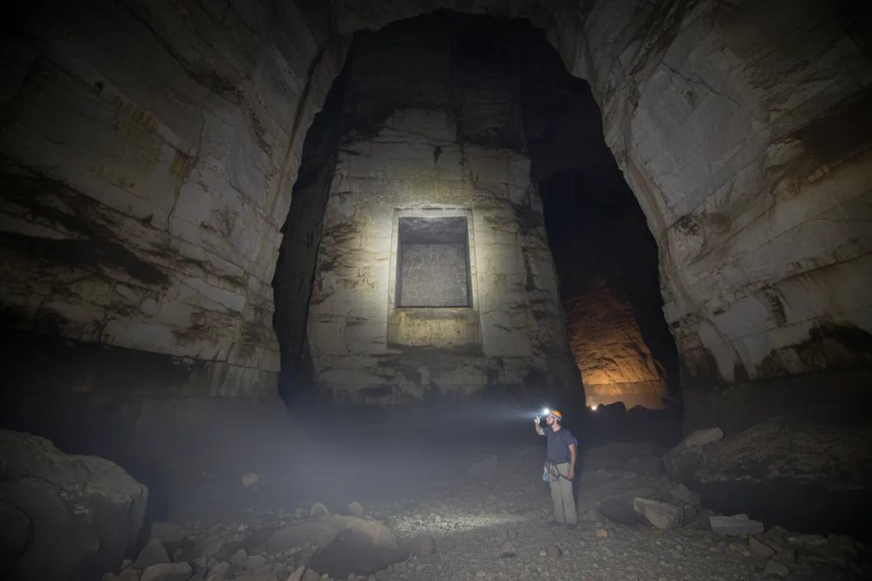 Inside Cueva de los Tayos, showing a vast, cathedral-like chamber with stalactites and stalagmites, illuminated by explorer's headlamps.