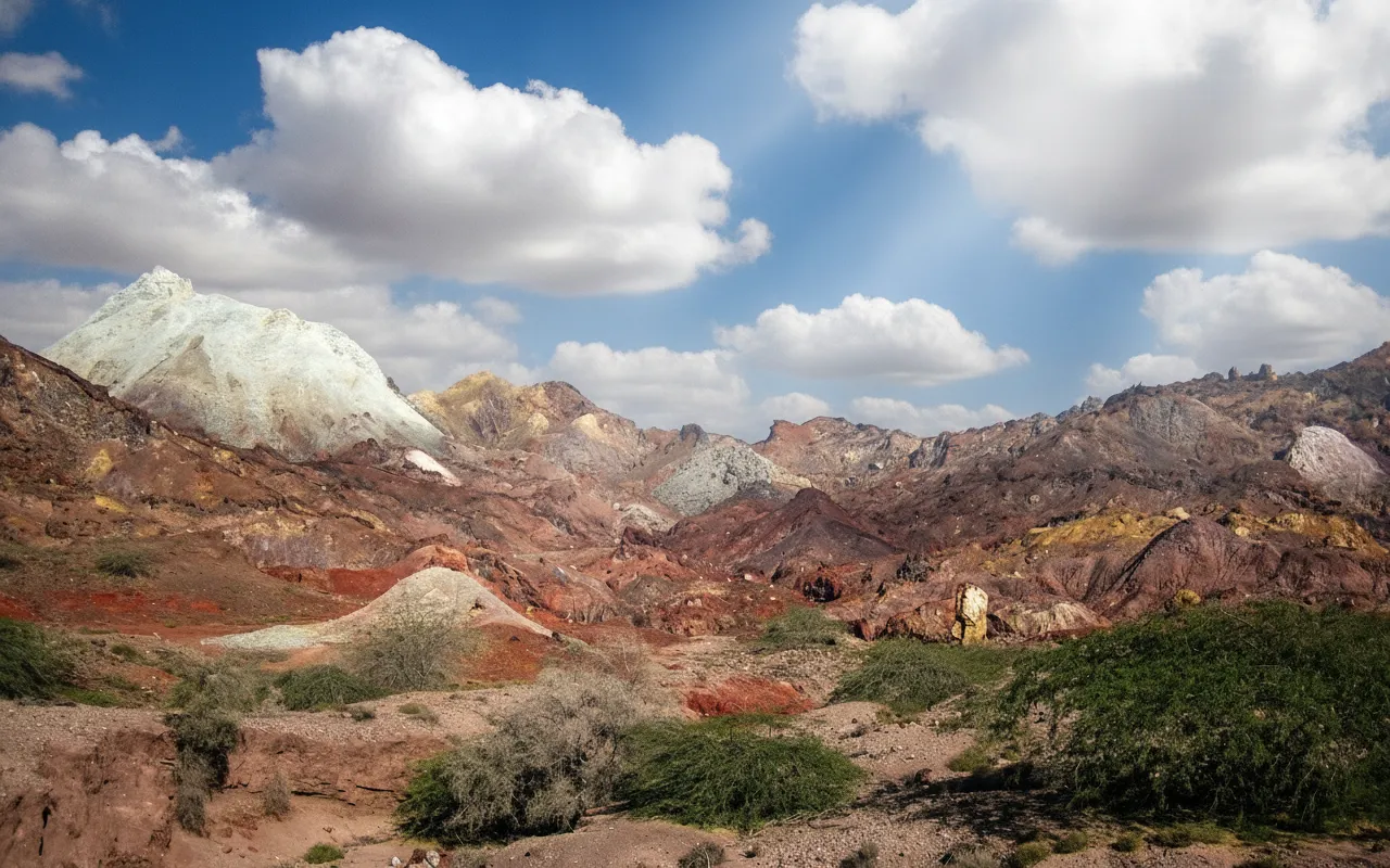 A local Hormuz islander riding a colorful tuk-tuk, a common mode of transport, passing by a vibrant red earth landscape.