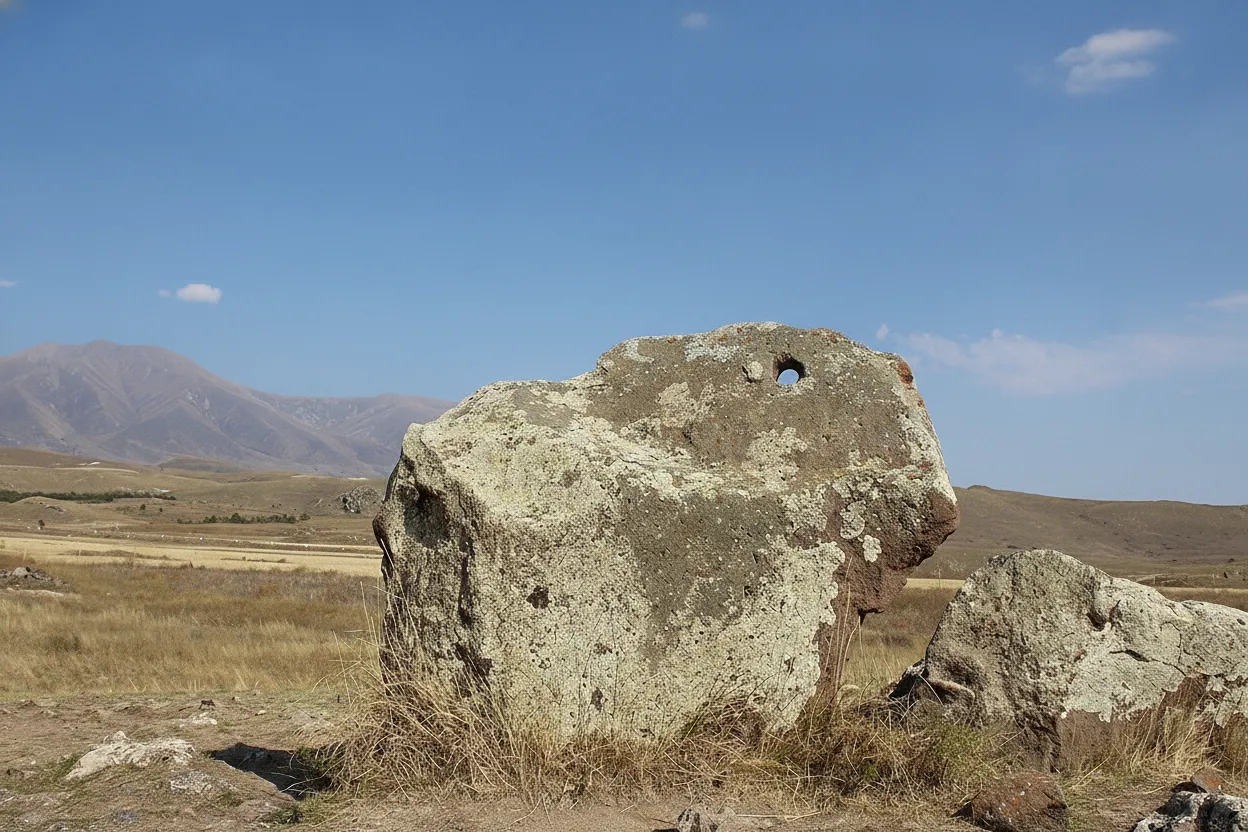 Close-up of a basalt standing stone at Karahunj, showing a perfectly drilled hole, with other stones in the background.