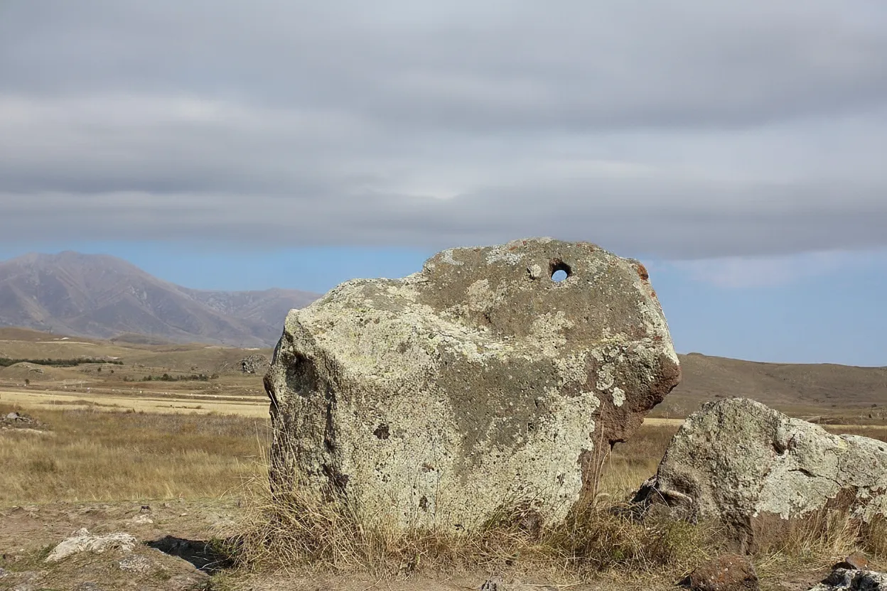 A traveler standing amongst the Karahunj stones, gazing towards the horizon under a dramatic sky, emphasizing the scale of the site.
