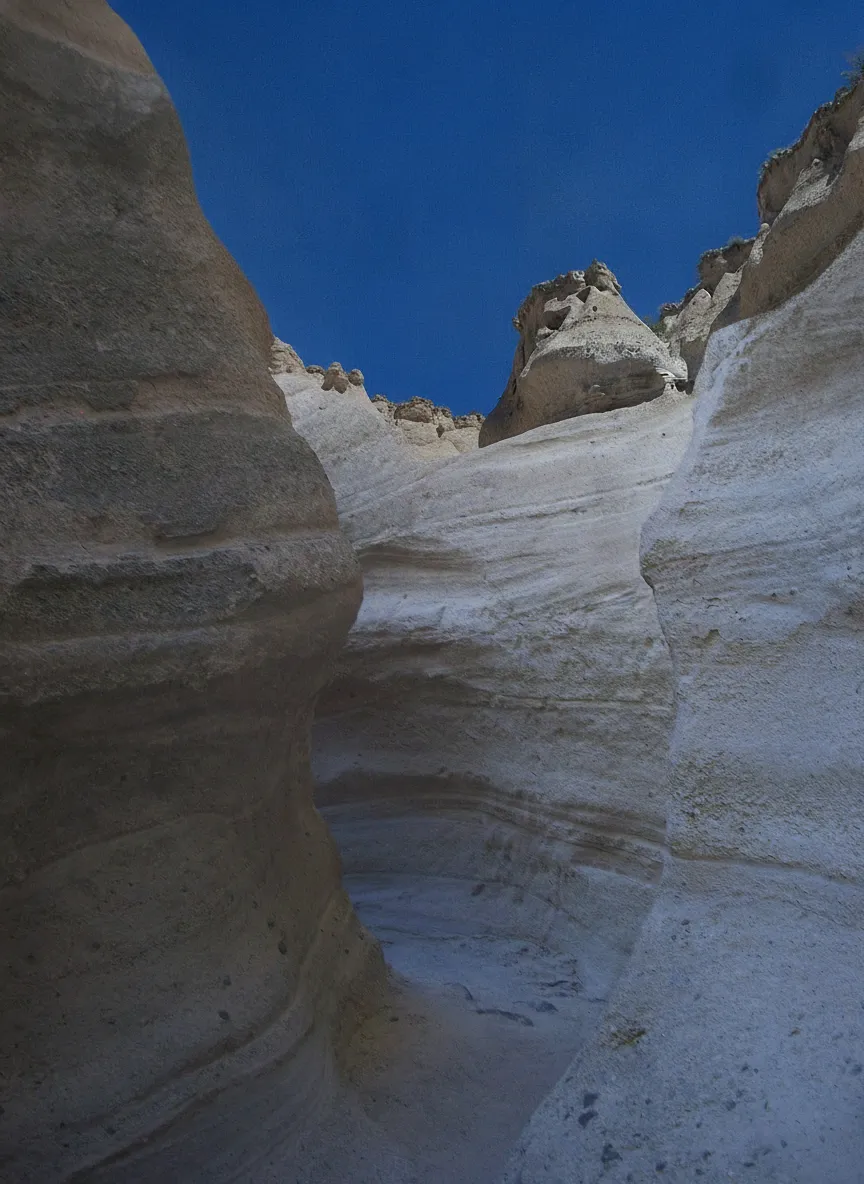 Close-up of a tent rock formation, showing the soft pumice cone topped with a harder, balancing boulder against a blue sky
