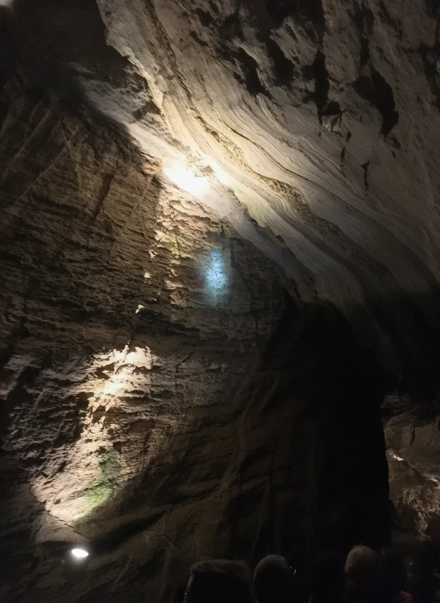 A rowboat glides silently across the crystal-clear, mirrored surface of Lac Souterrain de Saint-Léonard, reflecting ancient rock formations in the dimly lit underground cave.