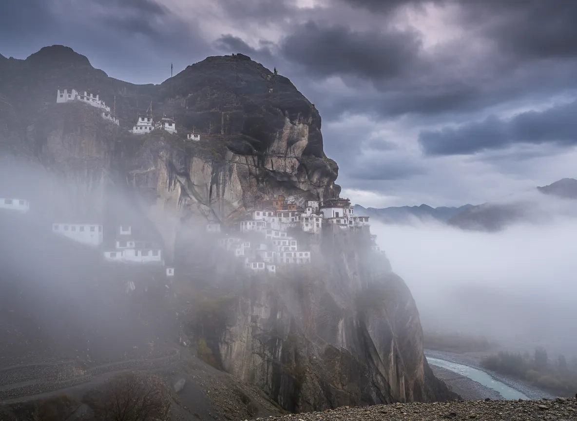 View from a window or balcony of Phugtal Monastery, showing the dramatic Zanskar mountains and the Lungnak River winding through the valley below.