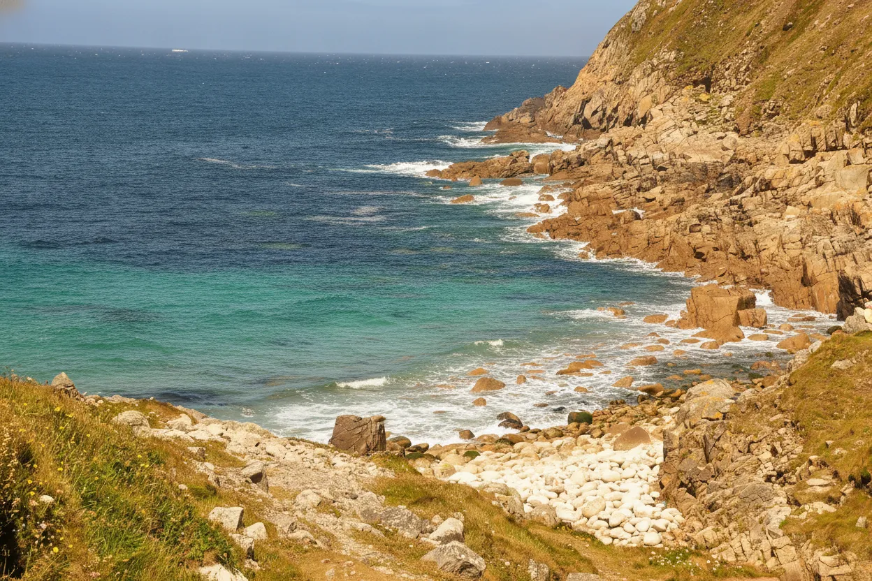 A dramatic shot of the coastline near Porth Nanven, showing rugged granite cliffs dropping into the Atlantic Ocean, with a hint of the 'dinosaur eggs' beach below.