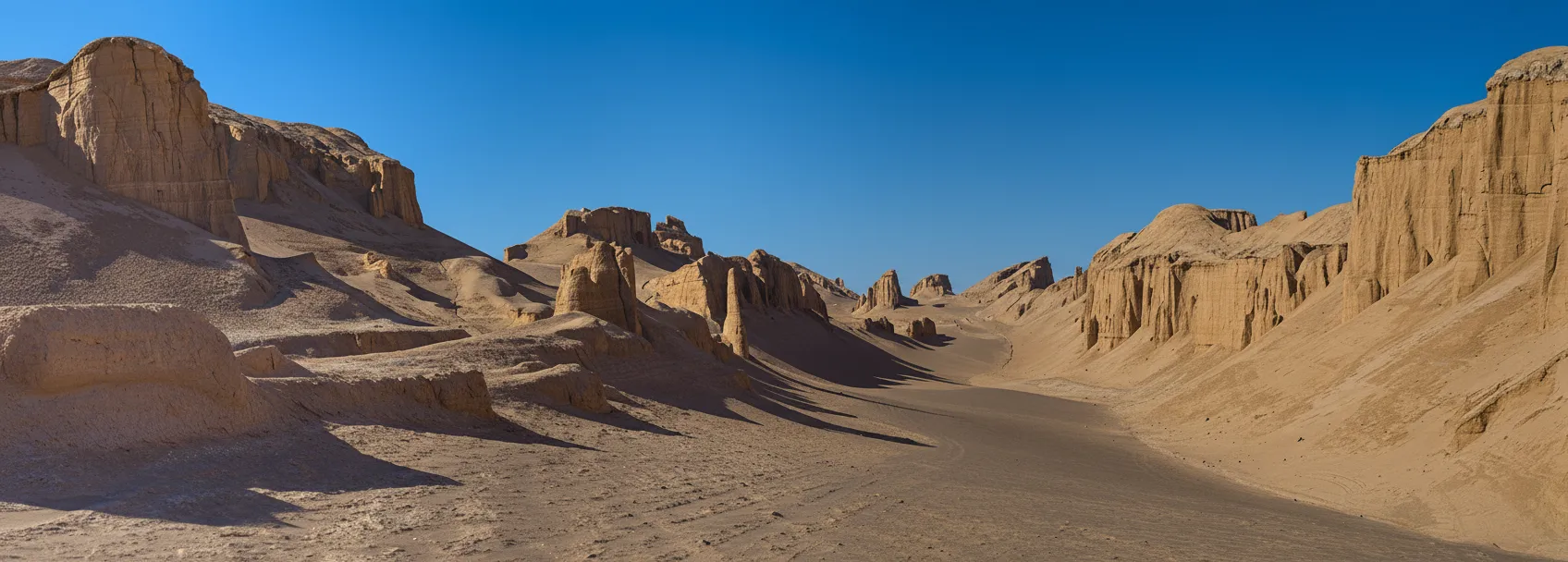 Panoramic view of Shahdad Kaluts in Iran, showing towering wind-sculpted rock formations under a clear blue sky.