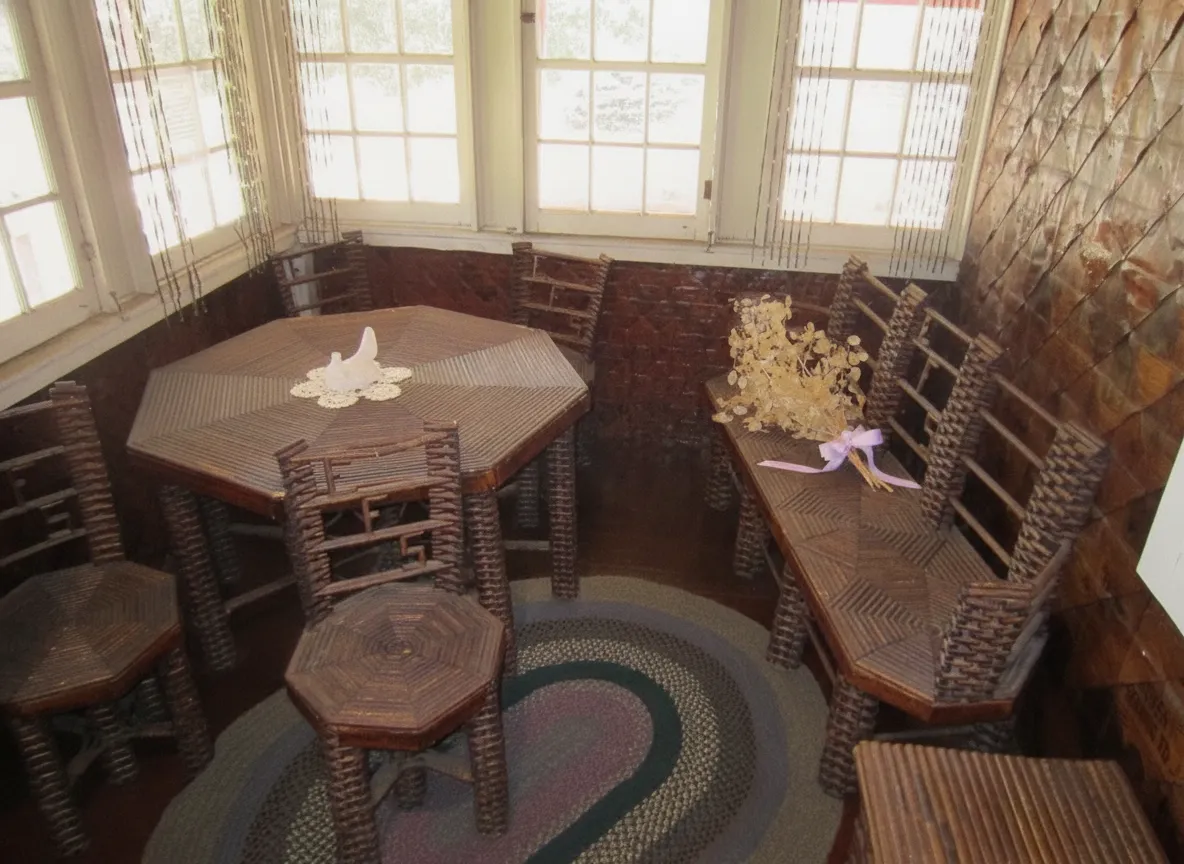 Interior view of The Paper House showing a chair and table made from rolled newspapers, with visible headlines and images.