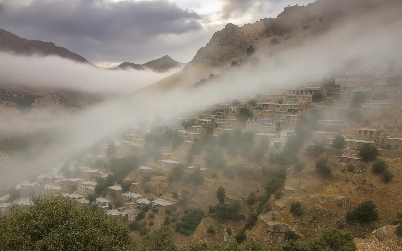 Panoramic view of Uraman Takht village nestled in the green Zagros Mountains, with a winding river in the valley below.