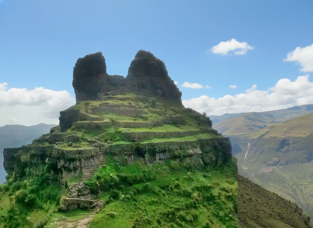 Waqrapukara fortress with its two prominent 'horns' jutting out from a cliff edge against a dramatic Andean sky.
